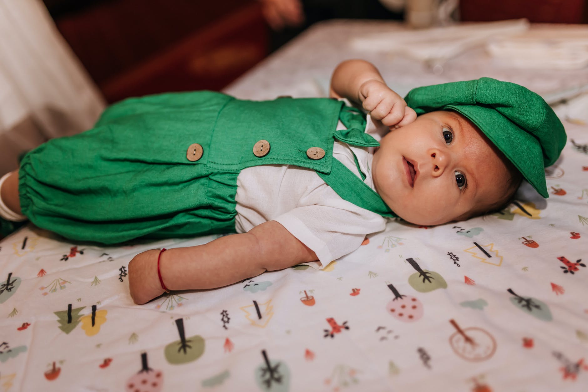newborn baby girl in green dress and cap lying on a bed