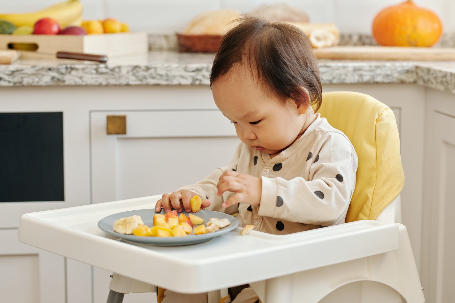 a toddler eating fruits sitting on the high chair