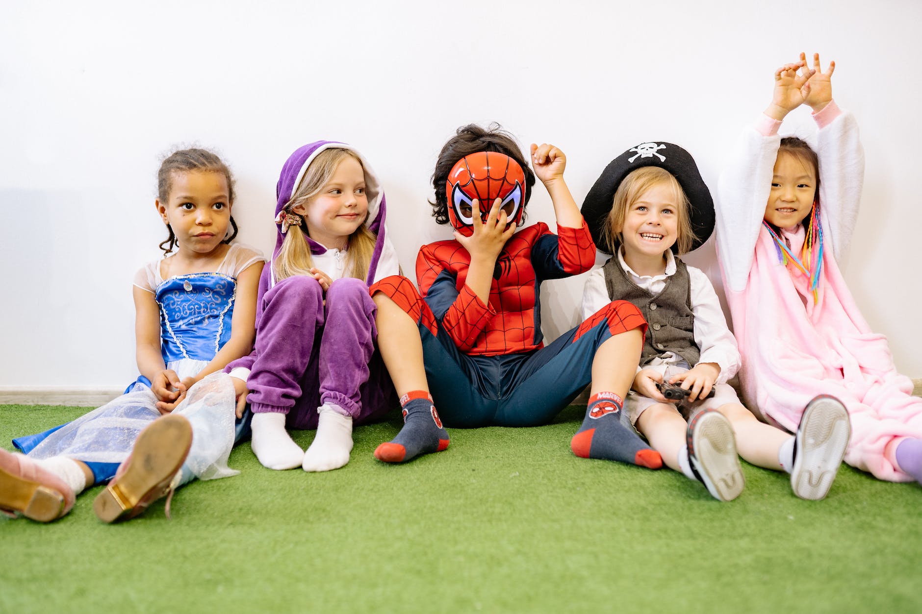 children sitting on green carpet wearing different costumes