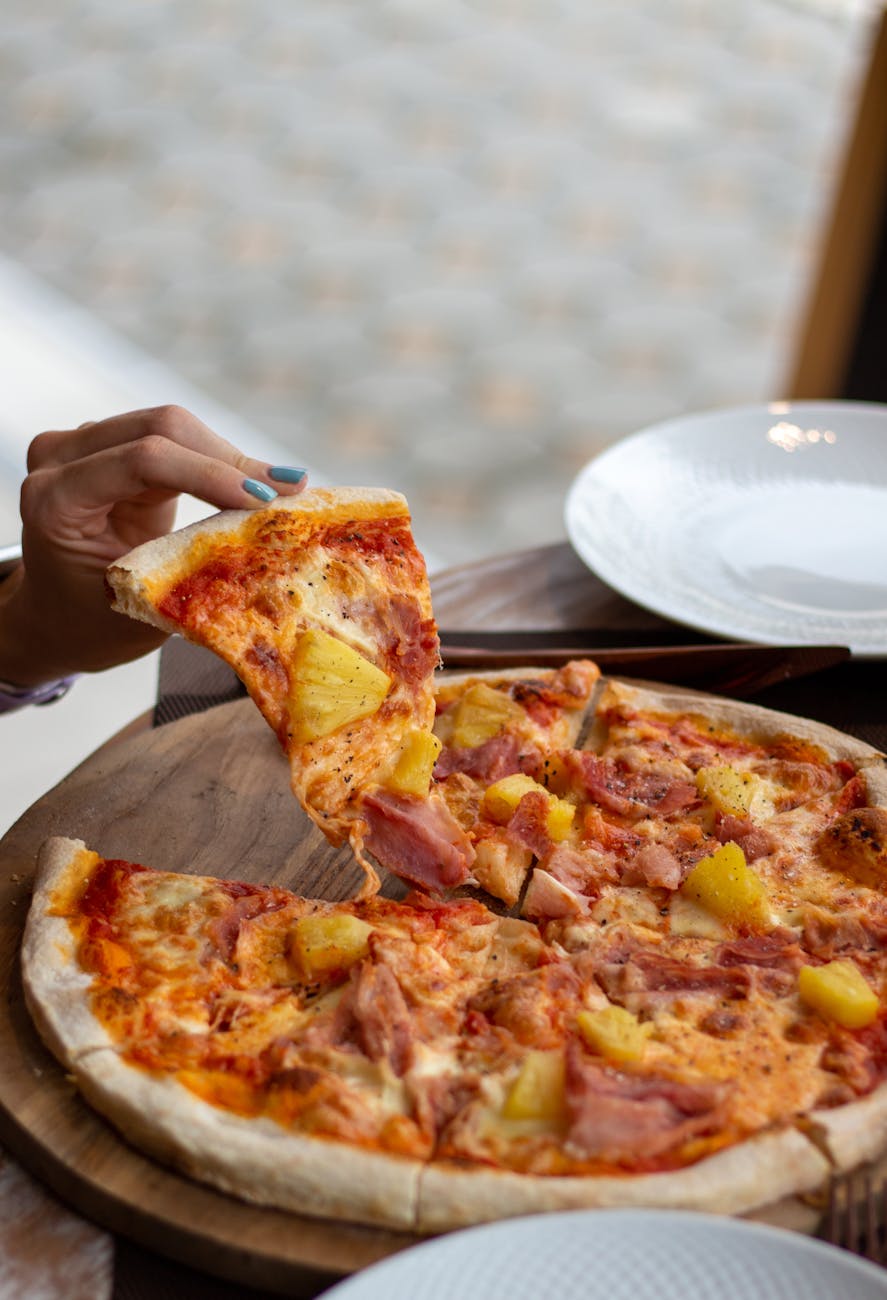 a person holding a slice of pizza on a wooden board