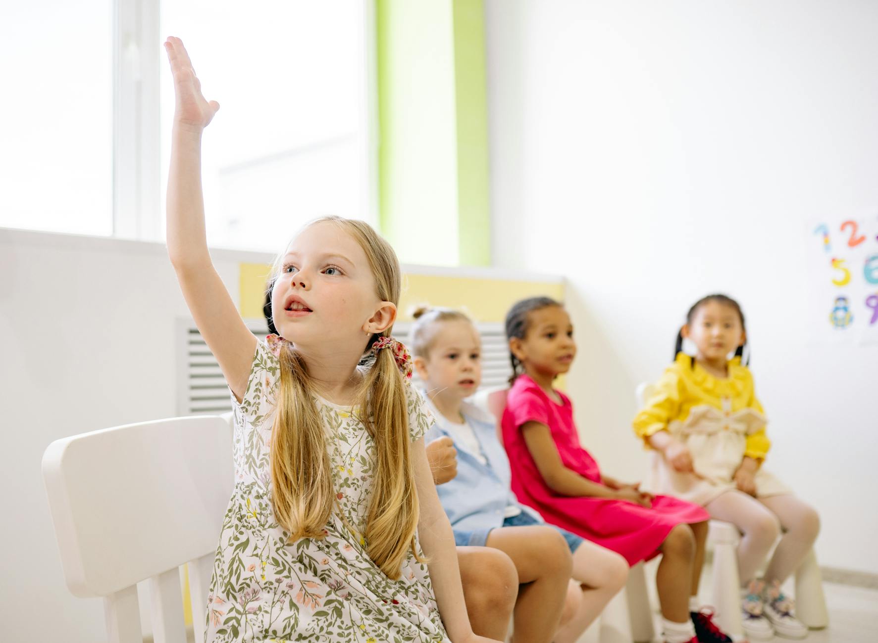 girl in white and black floral dress sitting on chair raising her hand